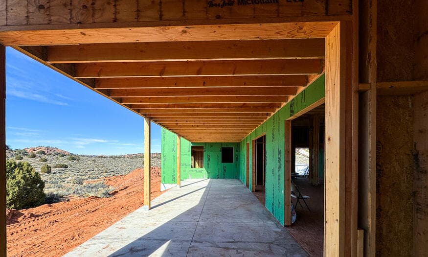 Framed covered walkway looking down a line of posts toward the red rock hillside