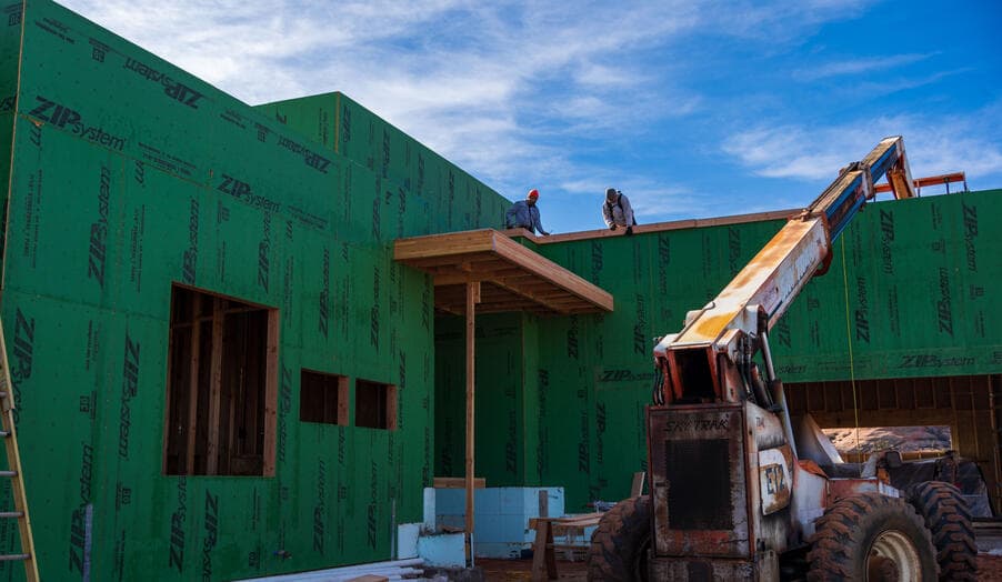 Two framers setting a beam on the roof line of a sheathed home in Moab