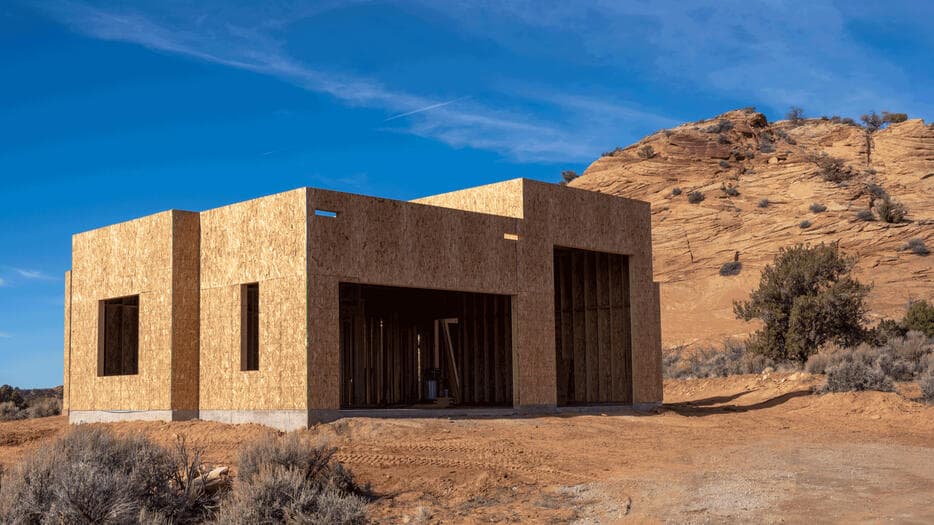 Sheathed exterior walls of a new home standing against a sandstone fin under a clear blue sky