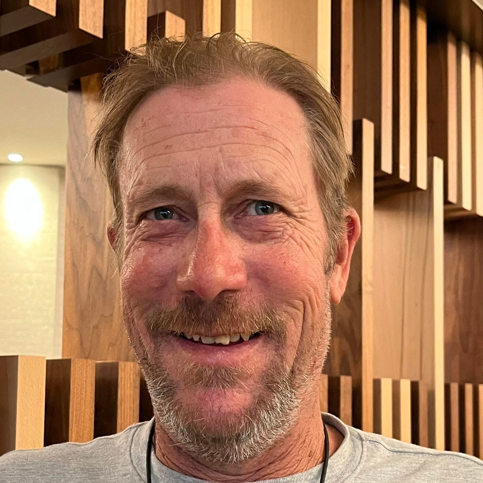 Troy Mecham, owner of Hammer and Hand Homes, smiling in front of a wood slat wall